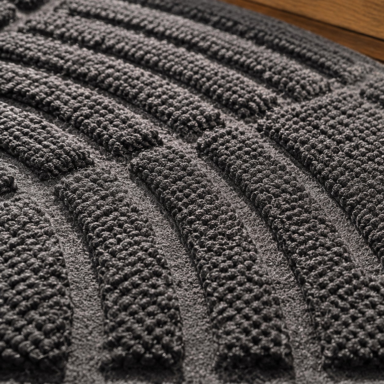 Close view of the dense looped texture and raised grooves on the dark gray door mat.
