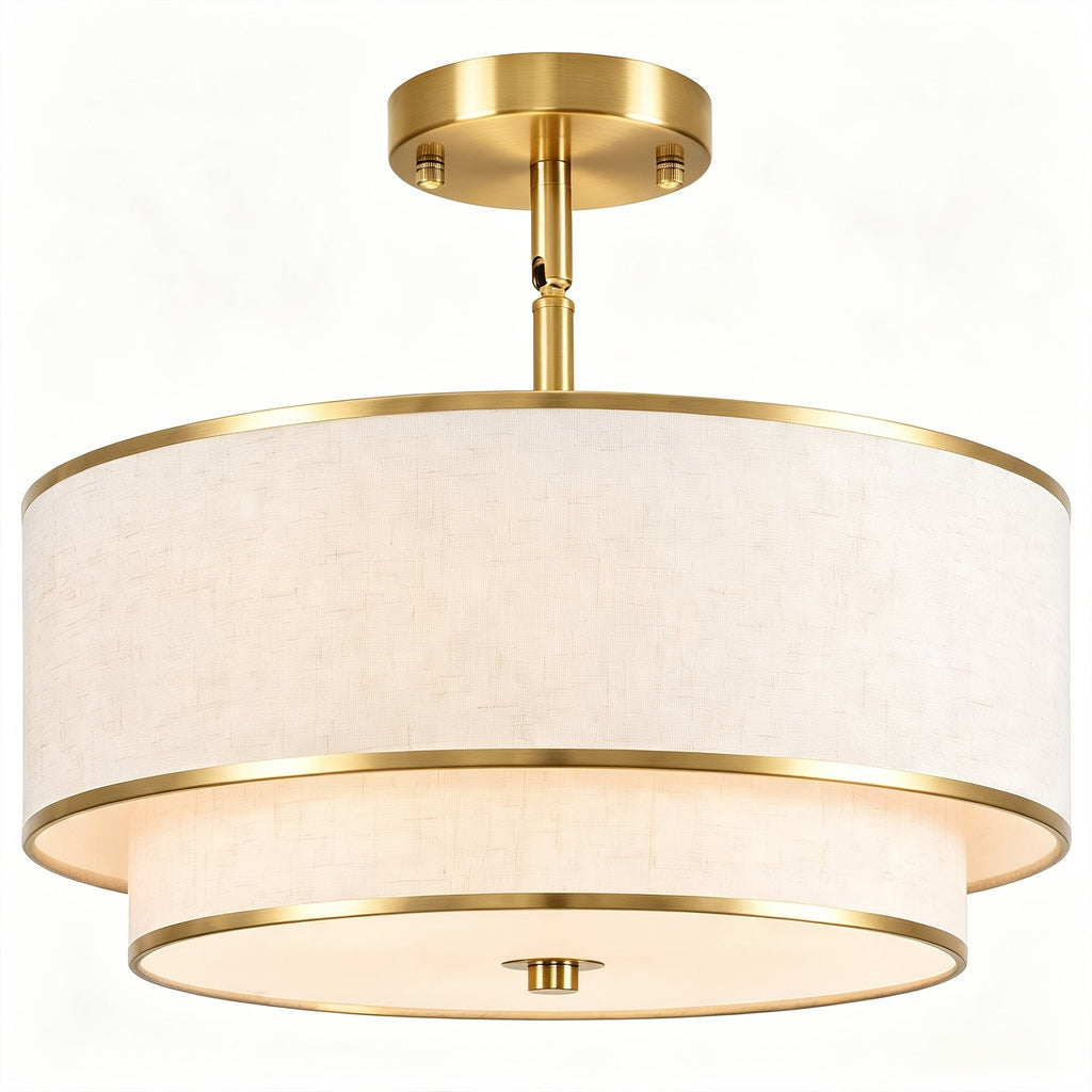 Gold drum ceiling light with a layered light colored linen shade against a plain background.
