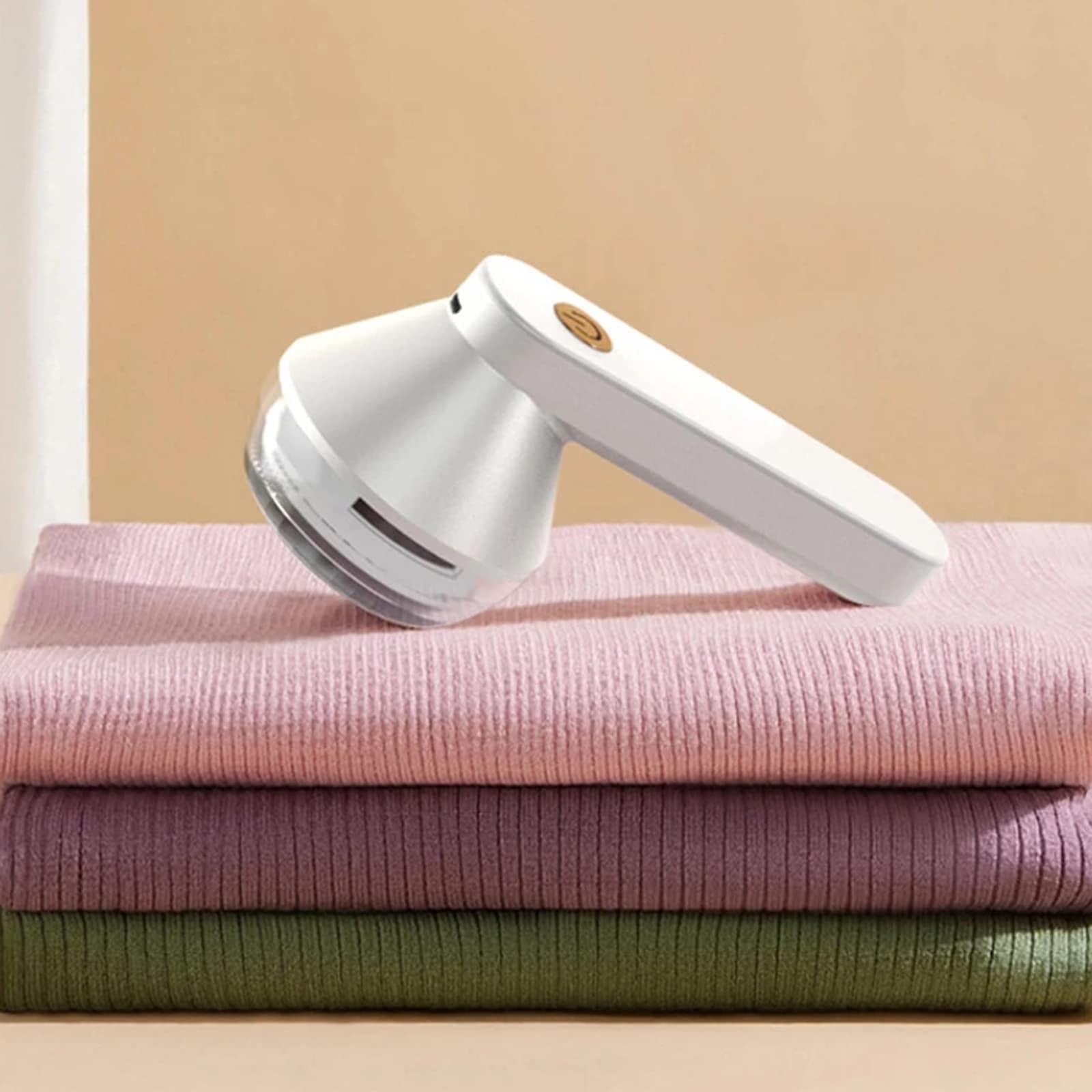 White rechargeable fabric shaver resting on folded knit clothing