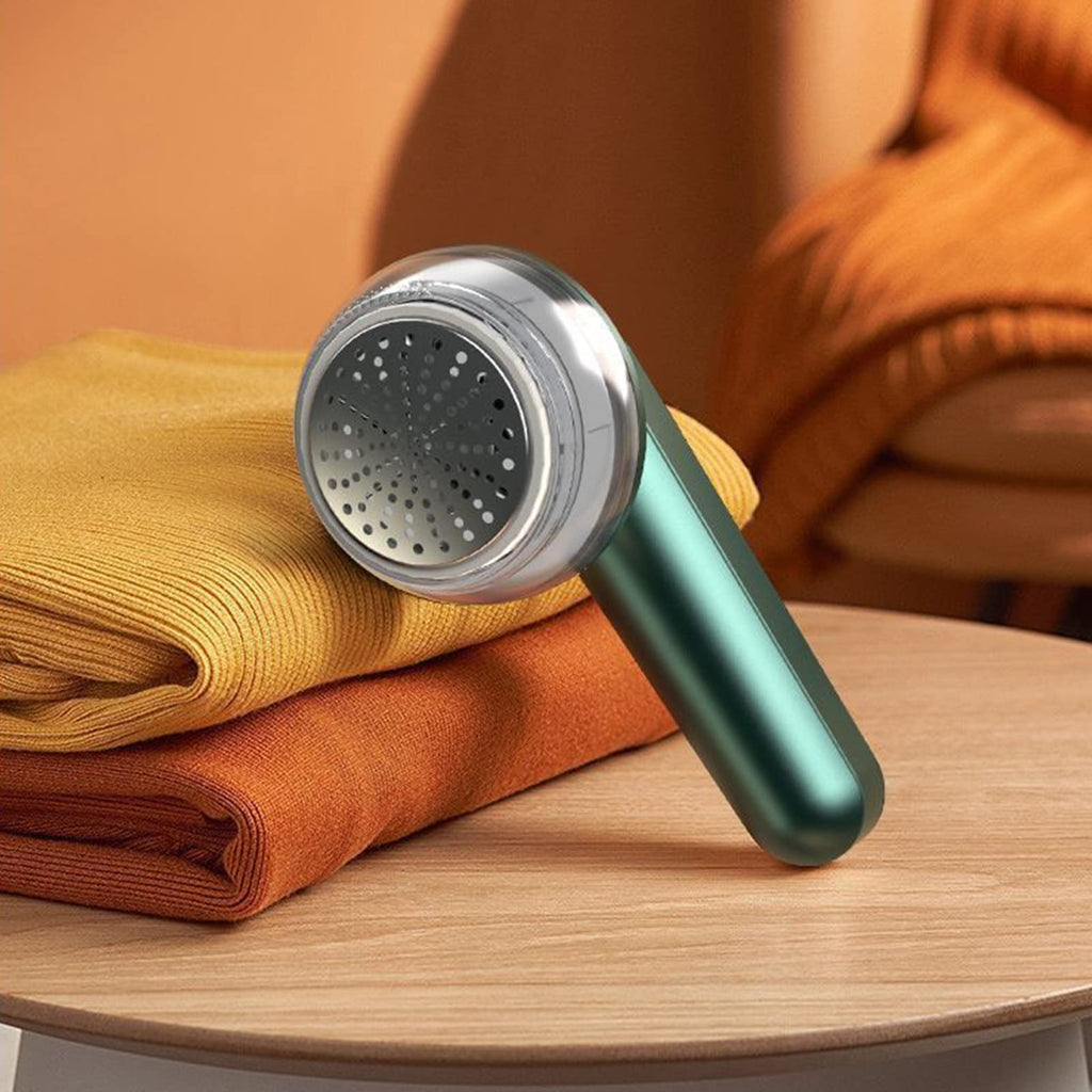 Green handheld fabric shaver with metal shaving screen beside folded clothing