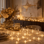Fairy string lights arranged across a dining table beside flowers.