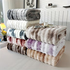 Faux fur throw blankets in several marbled colors stacked beside a bed.