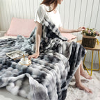A woman sitting at the edge of a bed with a gray faux fur throw blanket.