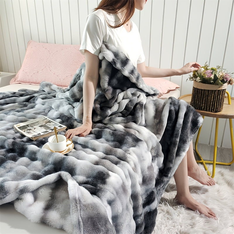 A woman sitting at the edge of a bed with a gray faux fur throw blanket.