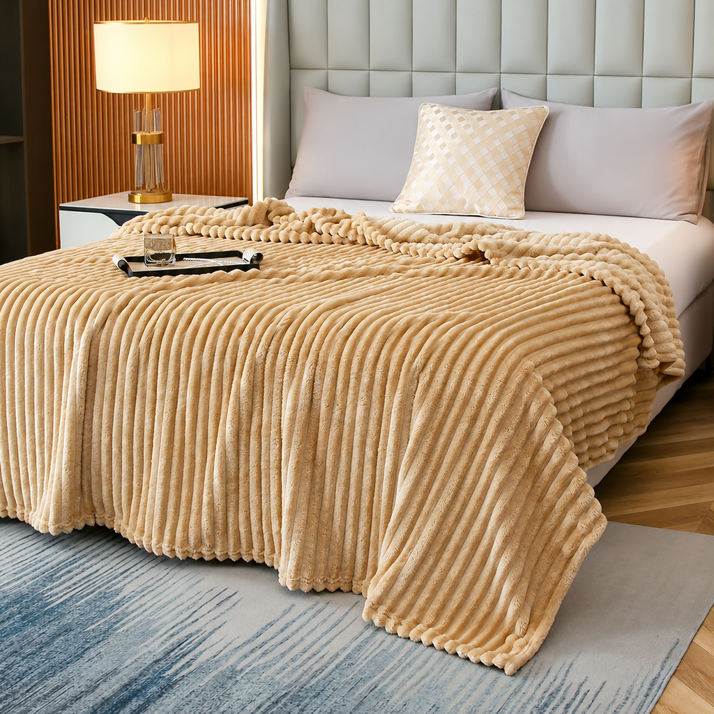 Beige faux fur throw blanket with raised stripes on a bed beside a lamp
