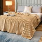 Beige faux fur throw blanket with raised stripes on a bed beside a lamp