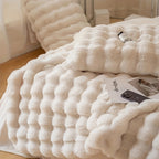 Close view of a white bubble textured faux fur throw blanket on a bed.