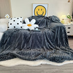 Dark gray faux fur throw blanket covering a bed with flower pillows.