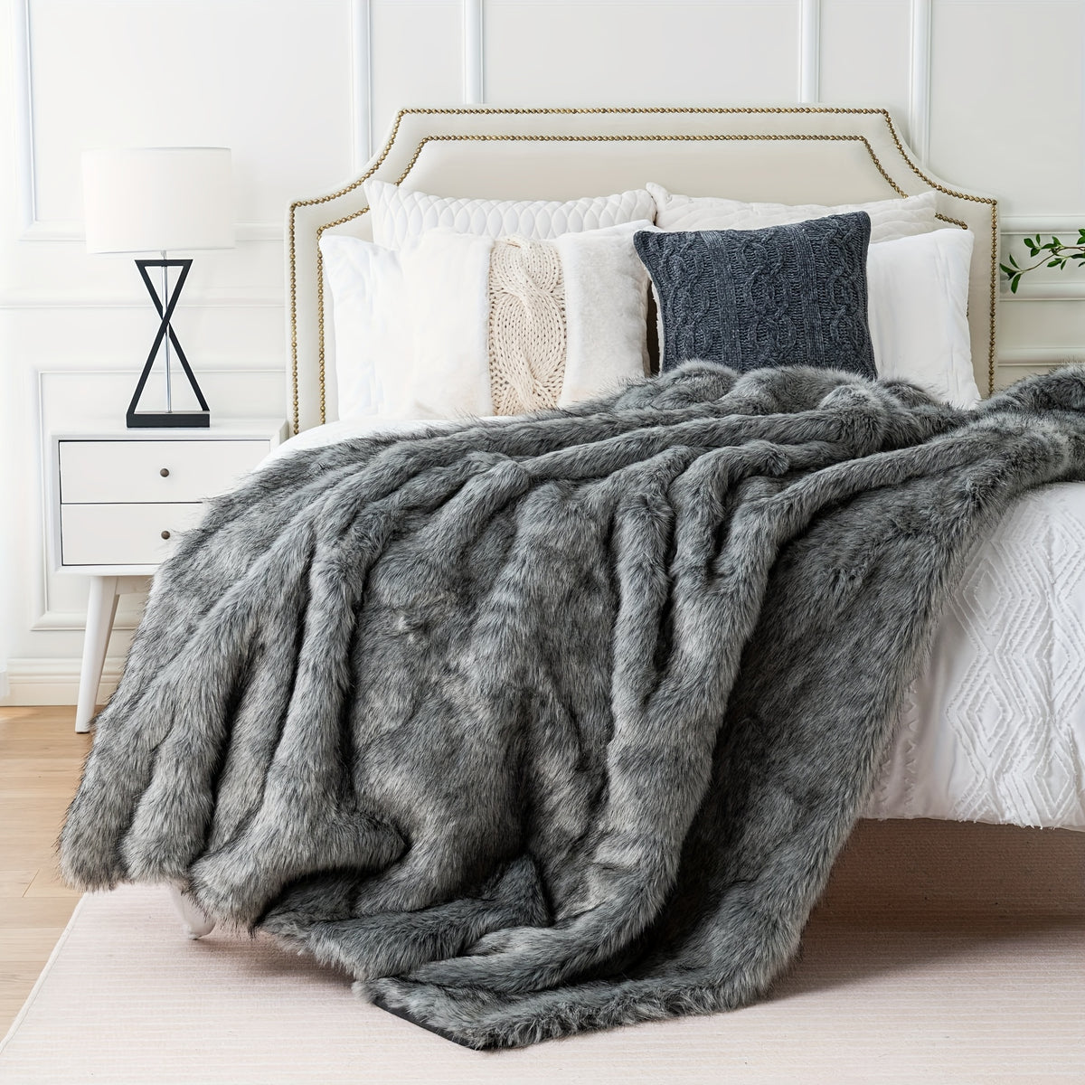 Gray faux fur throw blanket at the foot of a white bed.