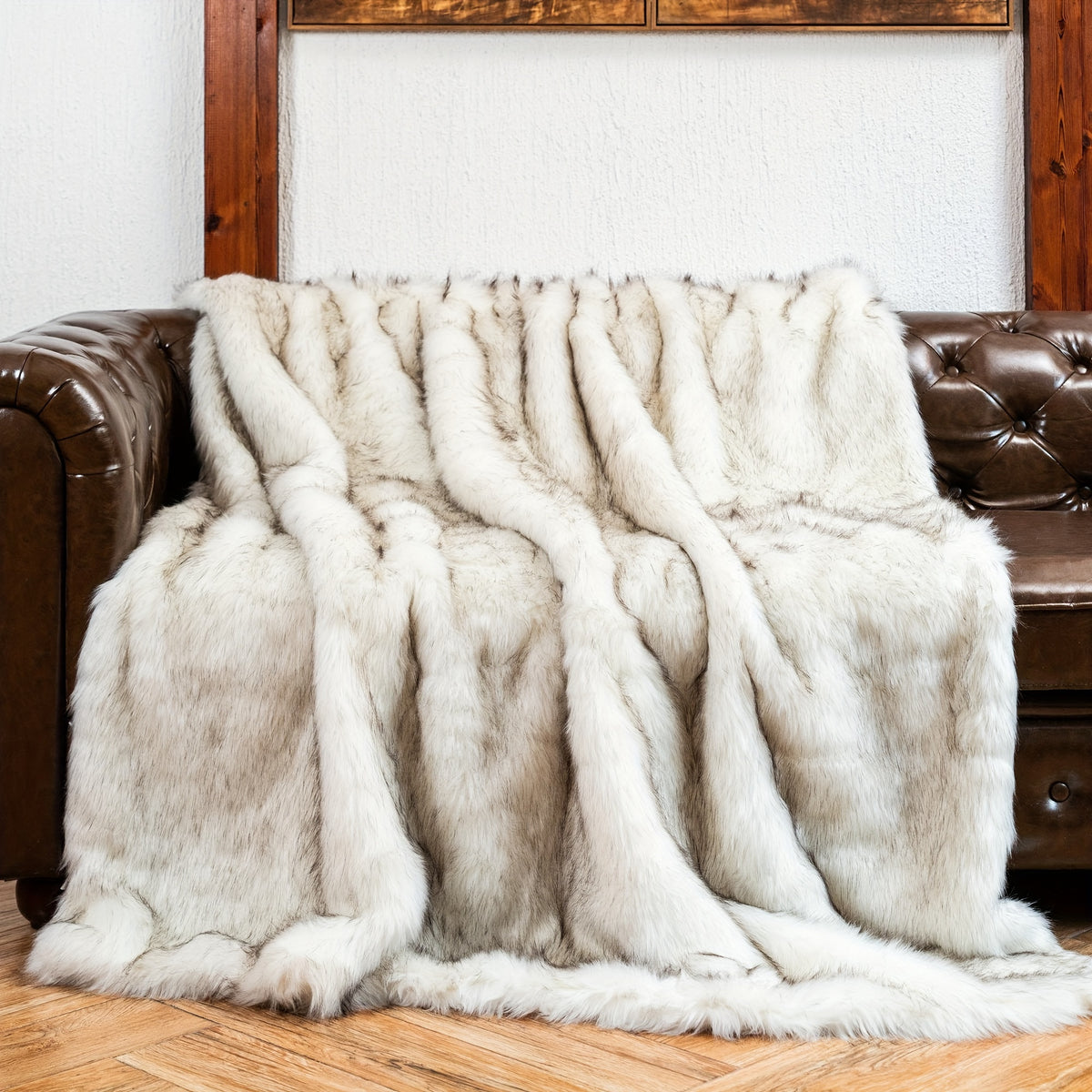 White tipped faux fur blanket draped over a brown leather couch.