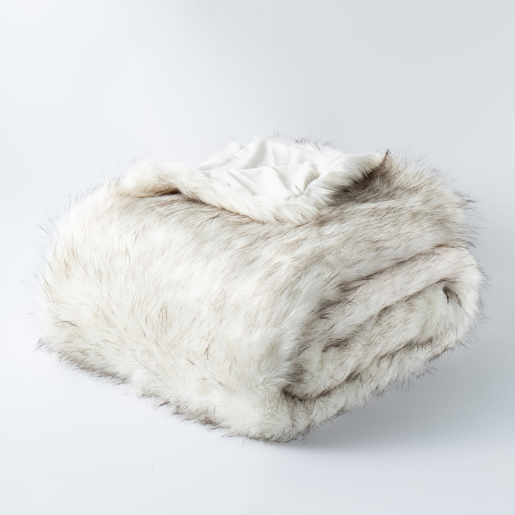 Folded white tipped faux fur blanket on a plain background.