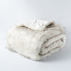 Folded white tipped faux fur blanket on a plain background.