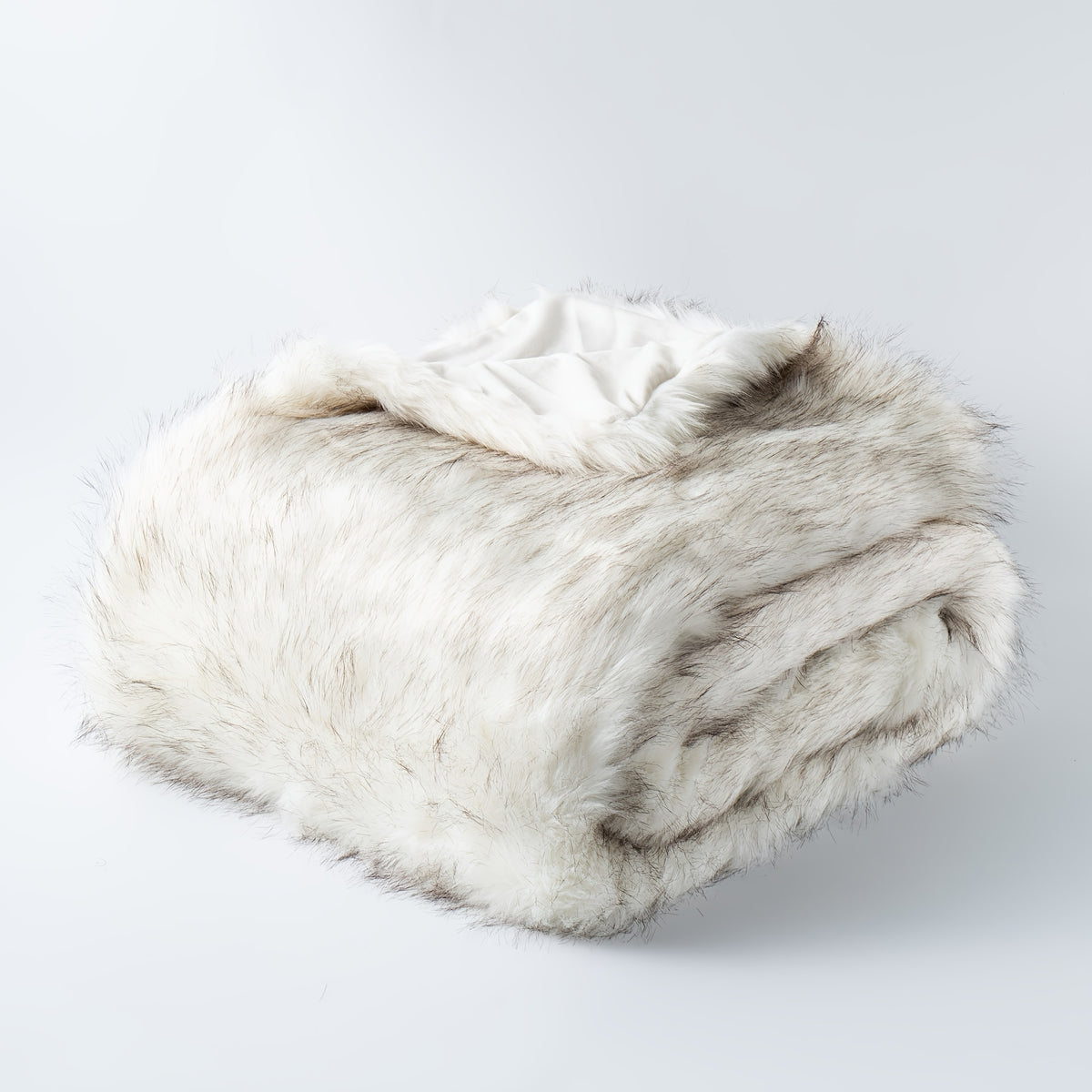 Folded white tipped faux fur blanket on a plain background.