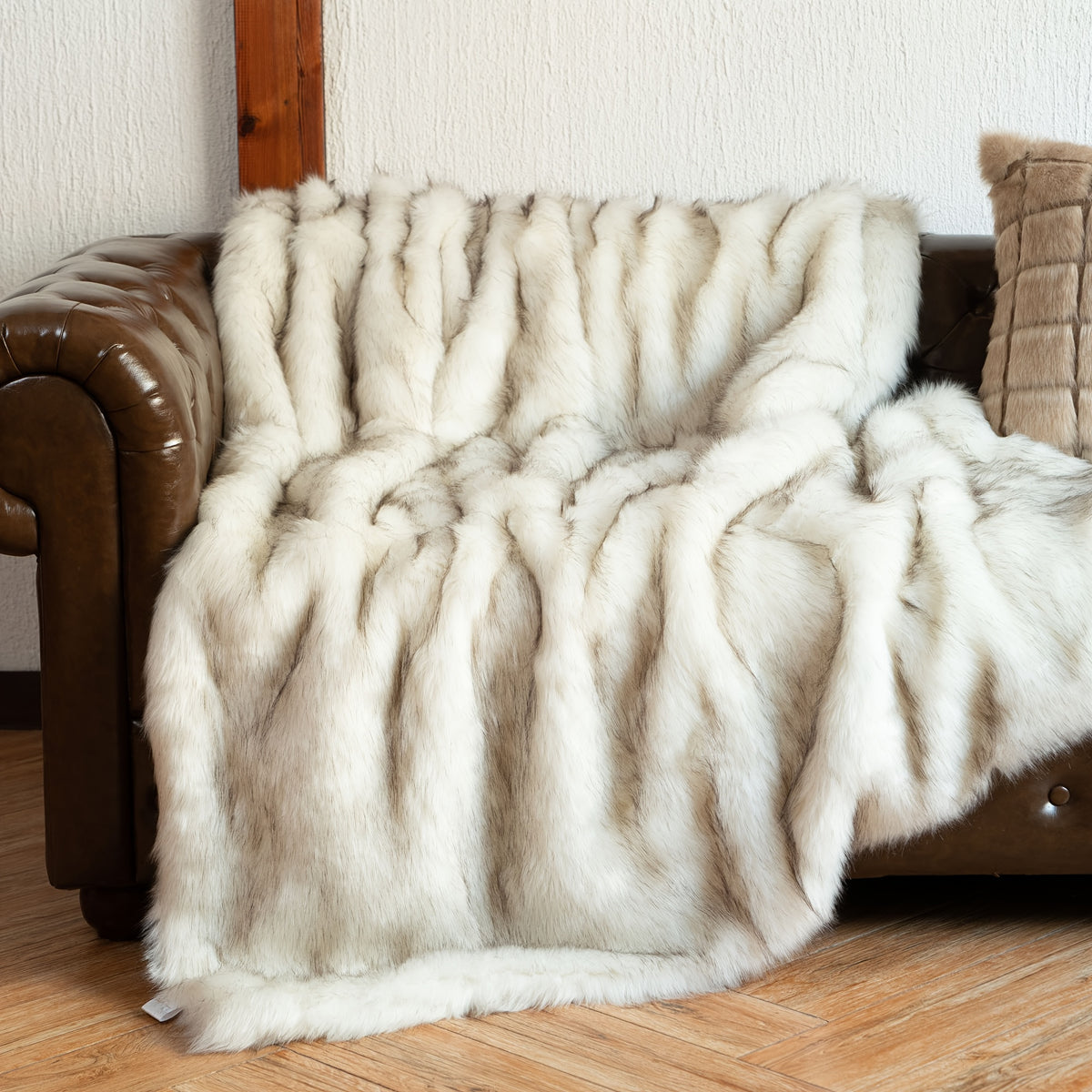White tipped faux fur blanket draped across a tufted leather couch.