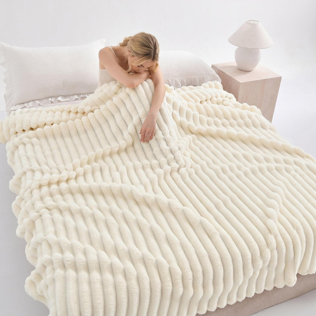 Woman resting on a bed under a white ribbed faux fur blanket.