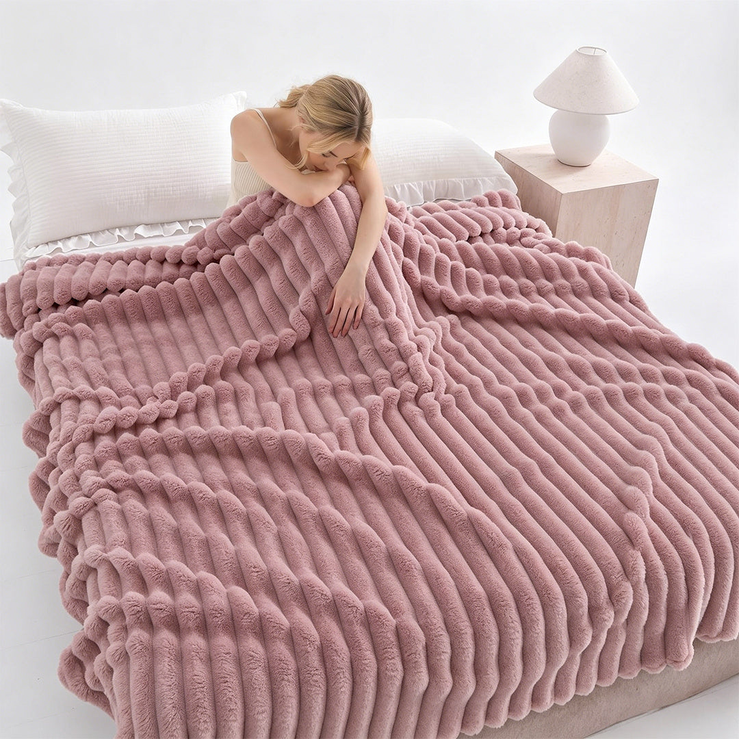 Woman resting on a bed under a pink ribbed faux fur blanket.