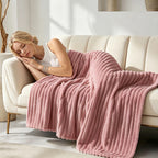 Woman resting on a couch under a pink ribbed faux fur blanket.