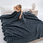 Woman resting on a bed under a dark blue gray ribbed blanket.