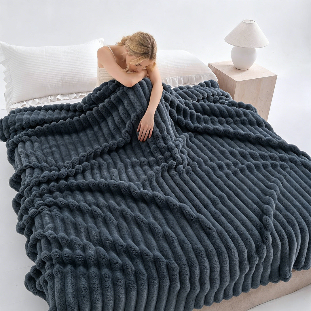 Woman resting on a bed under a dark blue gray ribbed blanket.