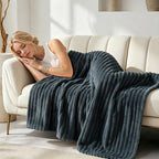 Woman resting on a couch under a dark blue gray ribbed blanket.