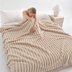 Woman resting on a bed under a khaki ribbed faux fur blanket.