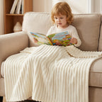 Child reading on a couch under a white ribbed blanket.