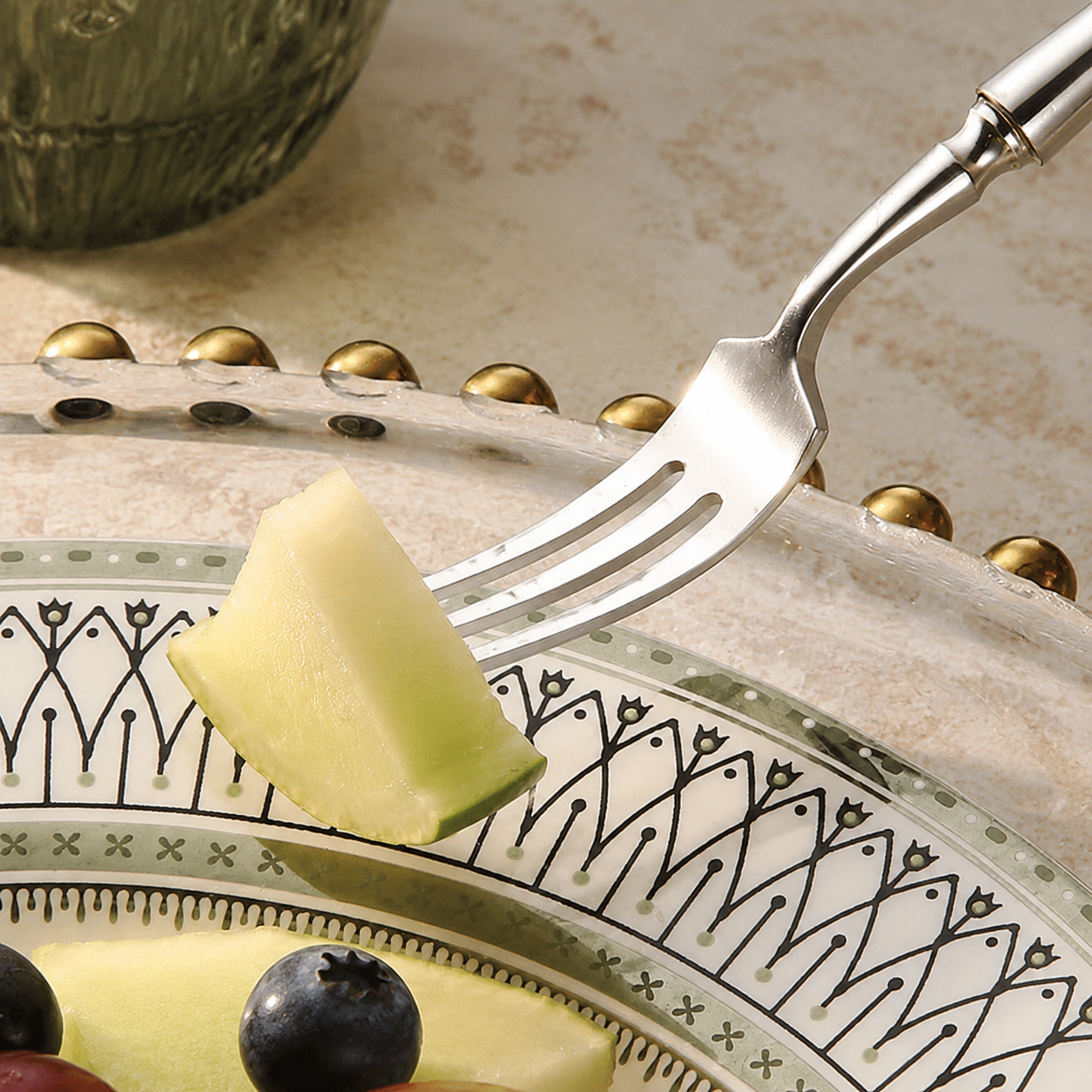 Flatware set fork lifting fruit from a patterned dinner plate in close view