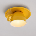 Yellow flush mount ceiling light with a glossy cup-shaped body and round glowing diffuser on a light ceiling.