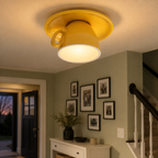 Yellow flush mount ceiling light glowing in a hallway with framed wall art and a console table.