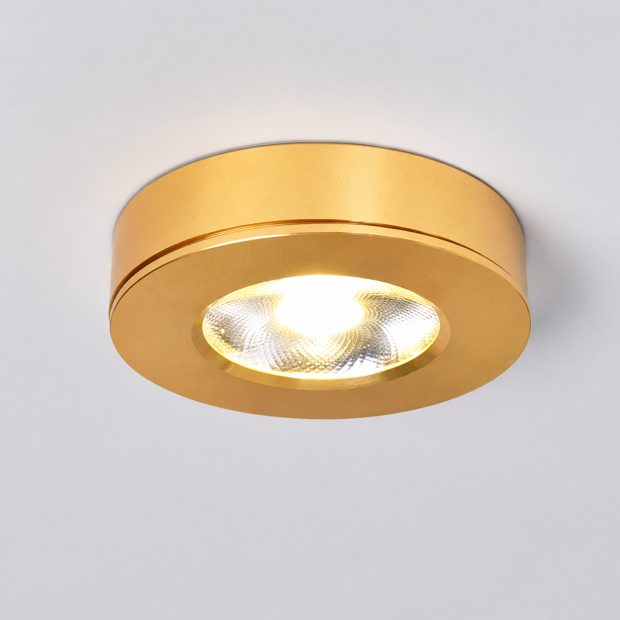 Gold flush mount ceiling light switched on against a plain light gray studio background.