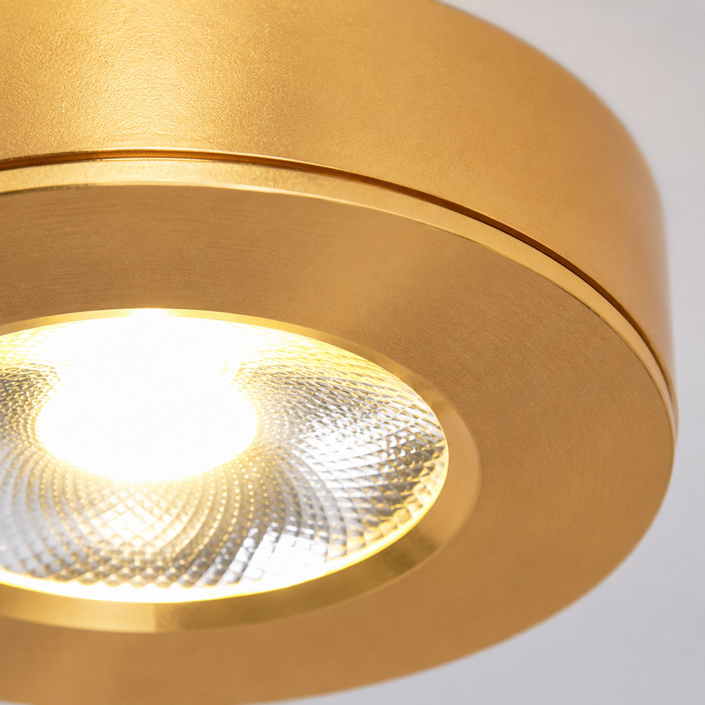 Close-up view of a gold flush mount ceiling light showing the illuminated center lens and rounded housing.