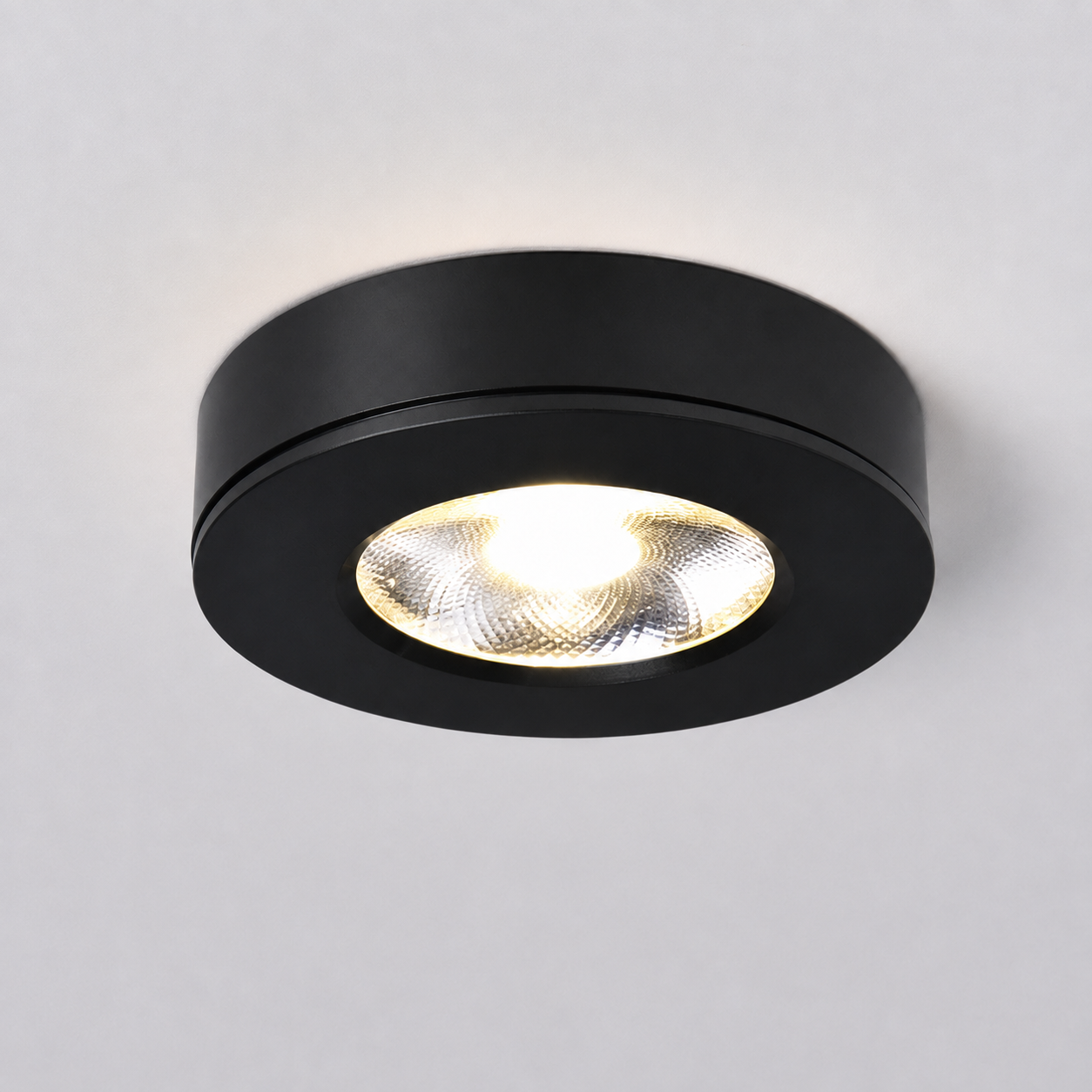 Black flush mount ceiling light switched on against a plain light gray studio background.
