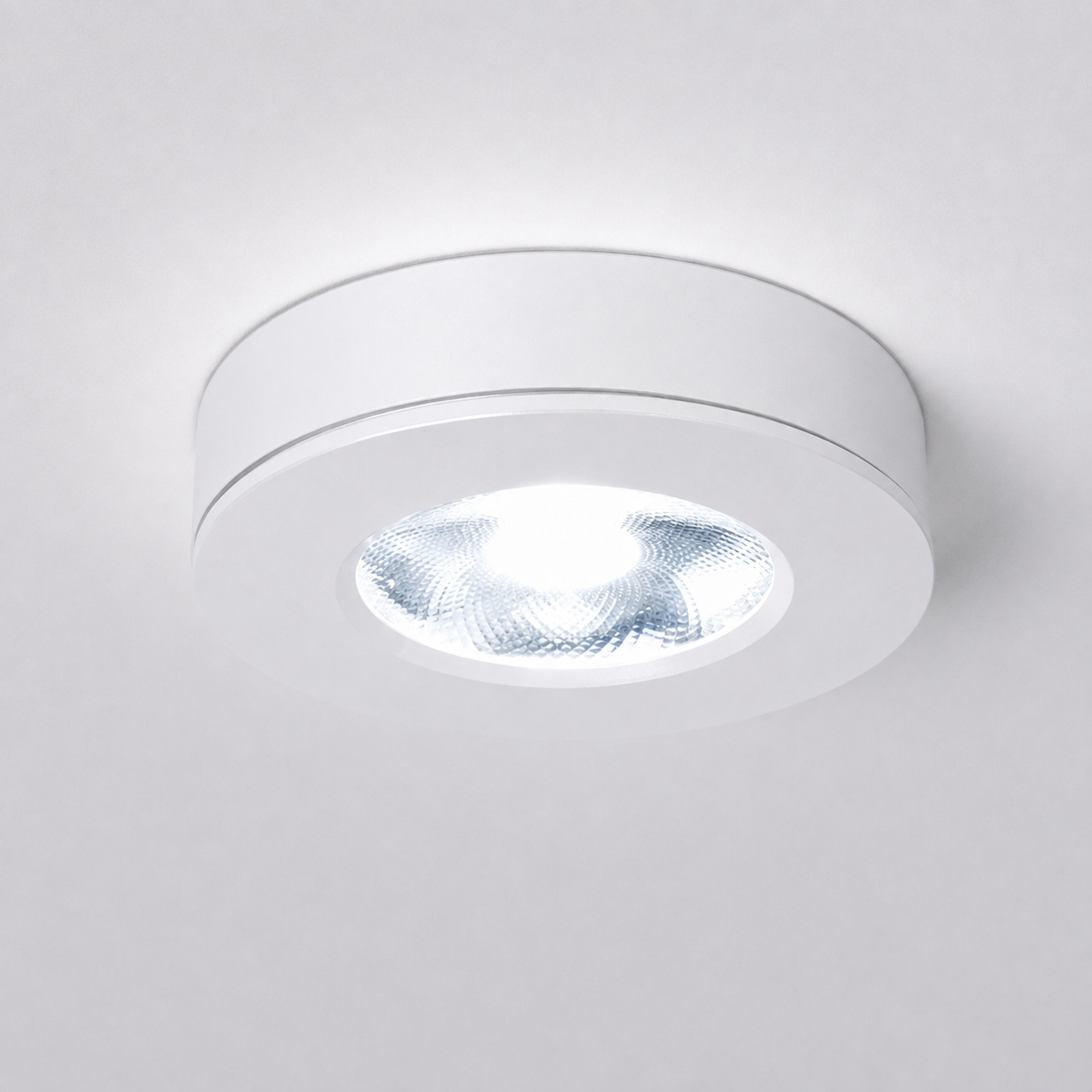 White flush mount ceiling light switched on against a plain light gray studio background.