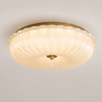 Flush mount ceiling light with a pleated translucent shade, warm glow, and small brass center detail.
