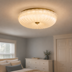 Flush mount ceiling light glowing above a bright bedroom with a dresser, window, chair, and plant.