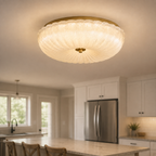 Flush mount ceiling light installed in a white kitchen above cabinets, counters, and a stainless steel refrigerator.