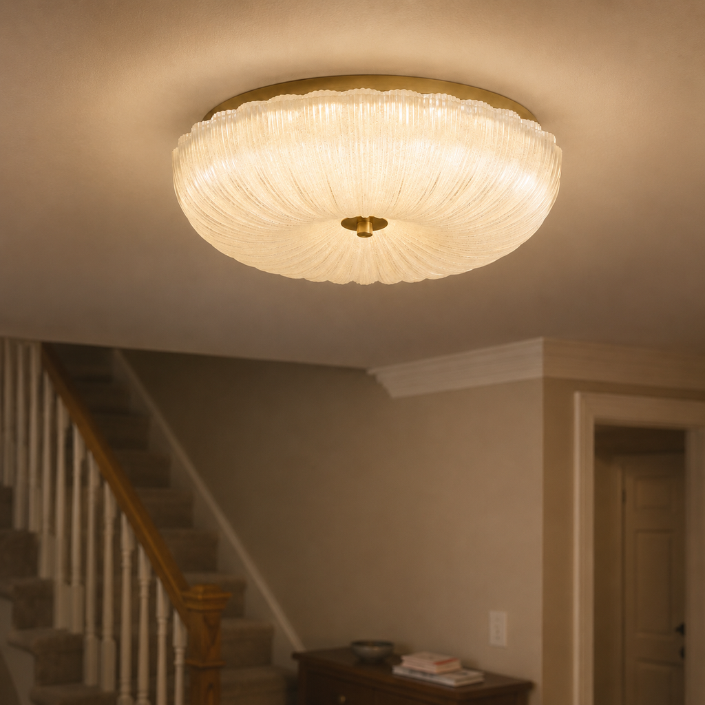 Flush mount ceiling light illuminating a neutral hallway beside a staircase and framed wall art.