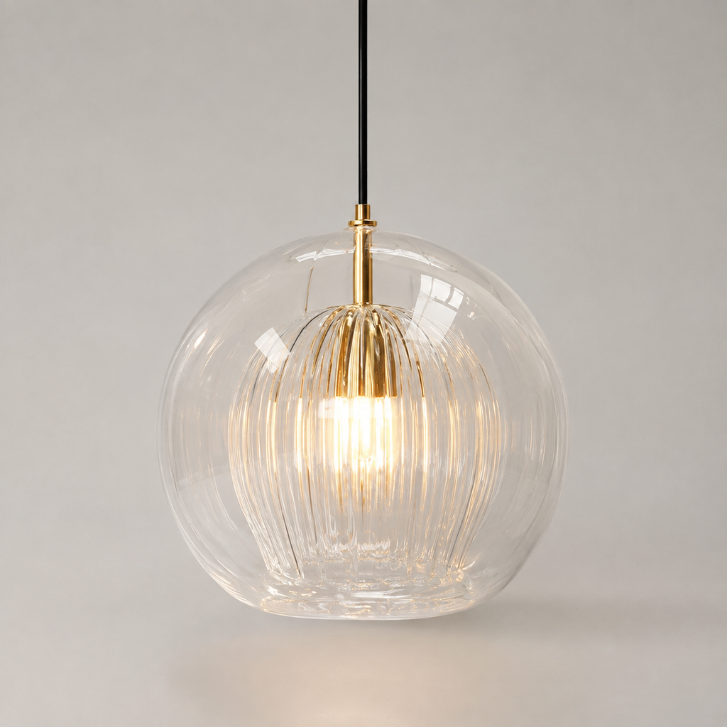 Clear ribbed glass pendant light with a warm glowing bulb and brass details on a neutral studio background.