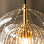 Close-up of a pendant light showing the brass stem, warm bulb, and ribbed clear glass shade.