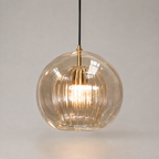 Amber ribbed glass pendant light with warm glow suspended against a soft beige studio background.