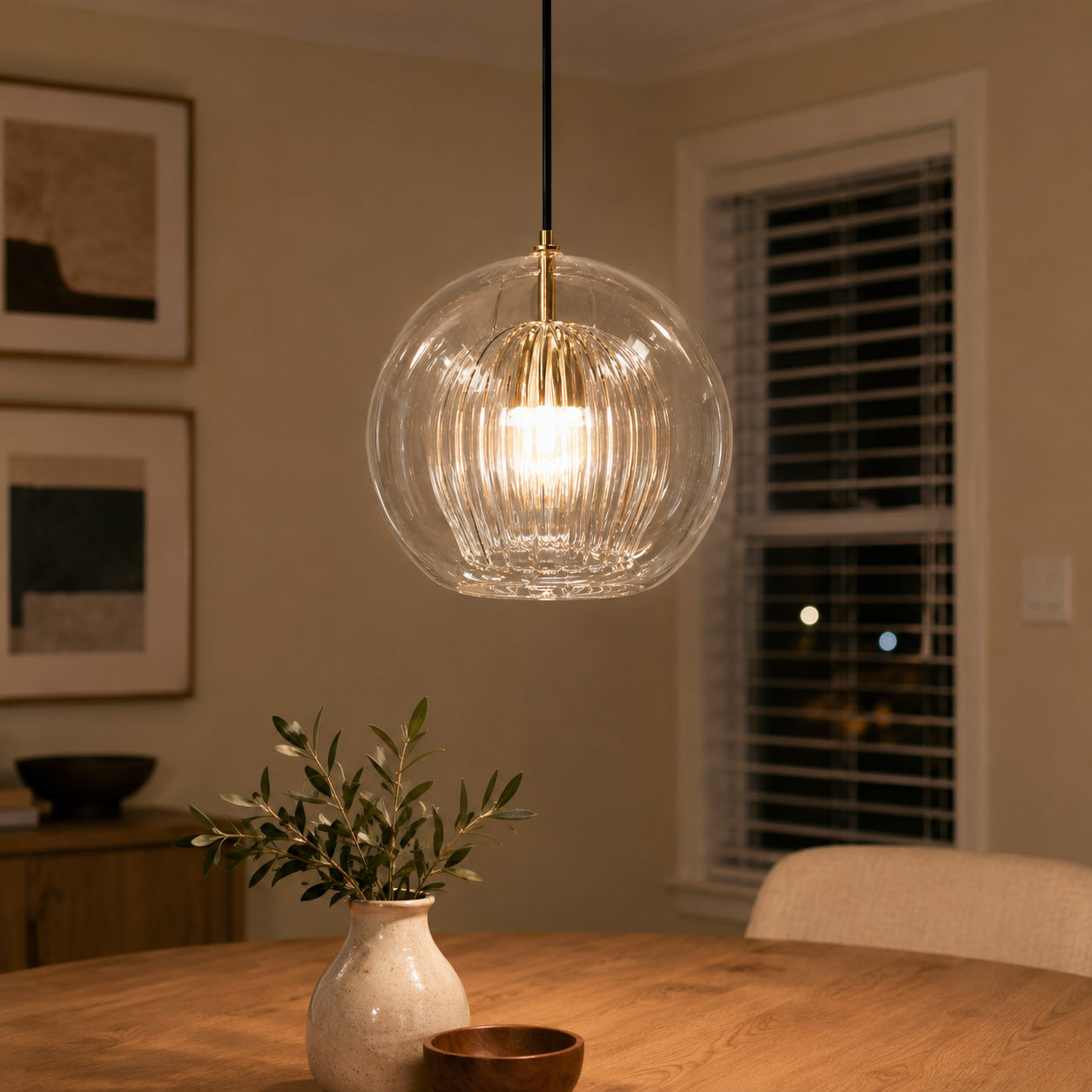 Warm pendant light hanging above a dining table in a softly lit room with framed wall art.