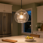 Clear glass pendant light glowing above a kitchen island with fruit and wood accents.
