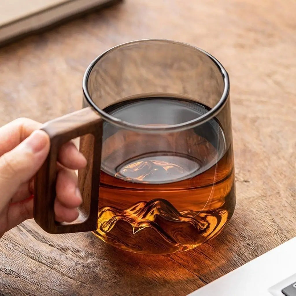 Smoky glass mug filled with tea, showing a mountain detail at its base