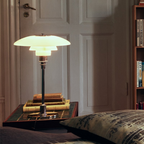 Glass table lamp with a pale illuminated shade on a bedside table