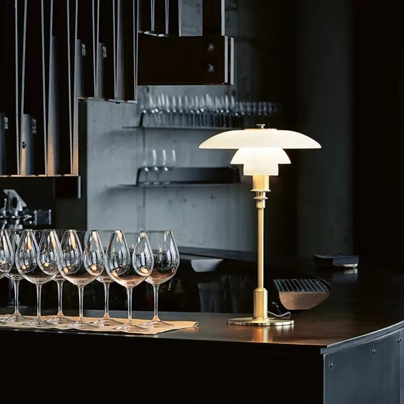 White glass table lamp with a gold finish beside drinking glasses