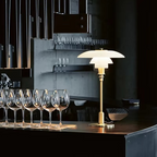 White glass table lamp with a gold finish beside drinking glasses