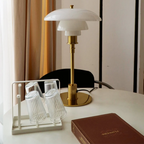 White glass table lamp with a gold finish beside a book and glasses