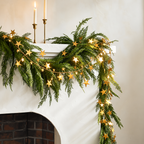 Gold star garland layered over greenery on a fireplace mantel.
