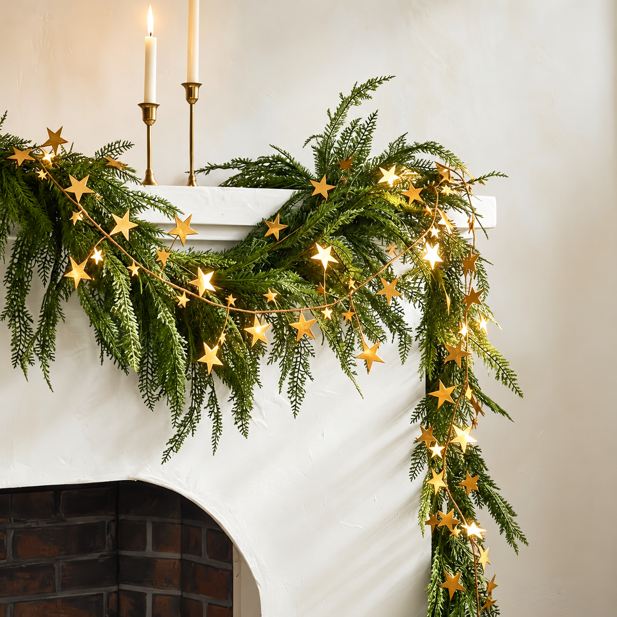 Gold star garland layered over greenery on a fireplace mantel.