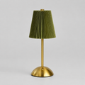 A modern table lamp with a pleated olive green fabric shade and a brushed gold metal base and stem, shown against a neutral light gray background.